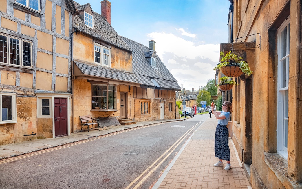 Cotswolds street scene with historic buildings and a person taking photos.
