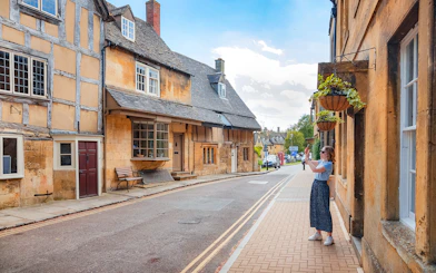 Cotswolds street scene with historic buildings and a person taking photos.
