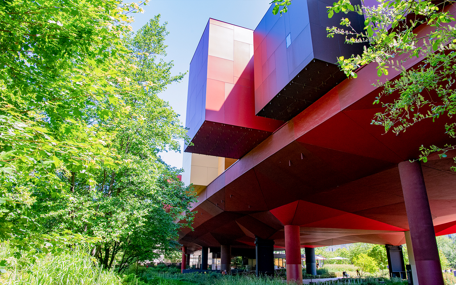 Musee du Quai Branly building with vibrant red and orange facade surrounded by greenery in Paris.