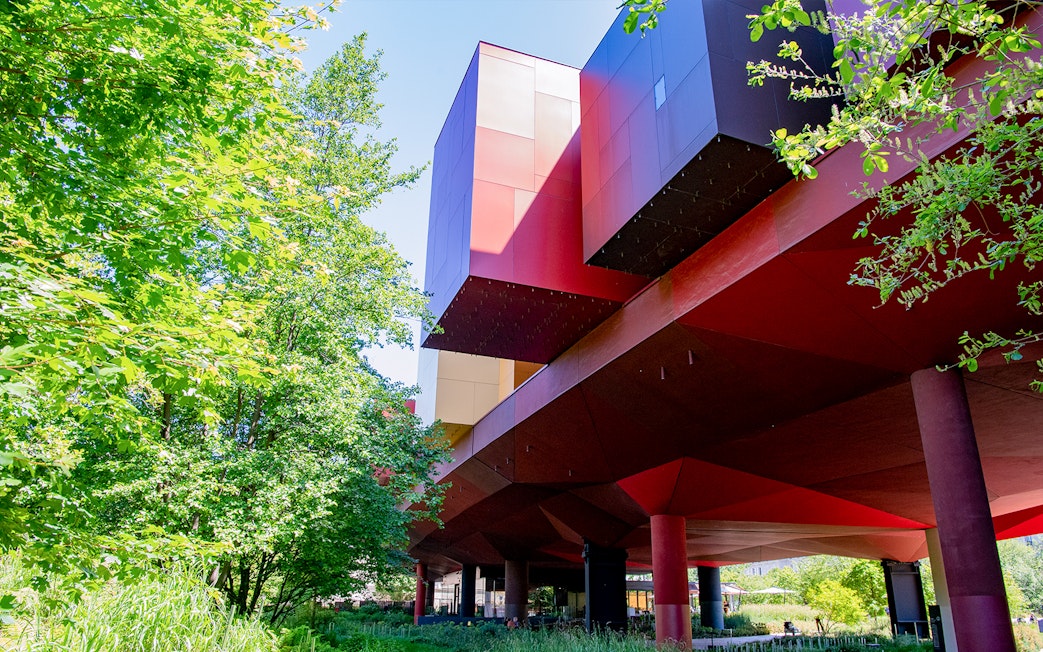 Musee du Quai Branly building with vibrant red and orange facade surrounded by greenery in Paris.