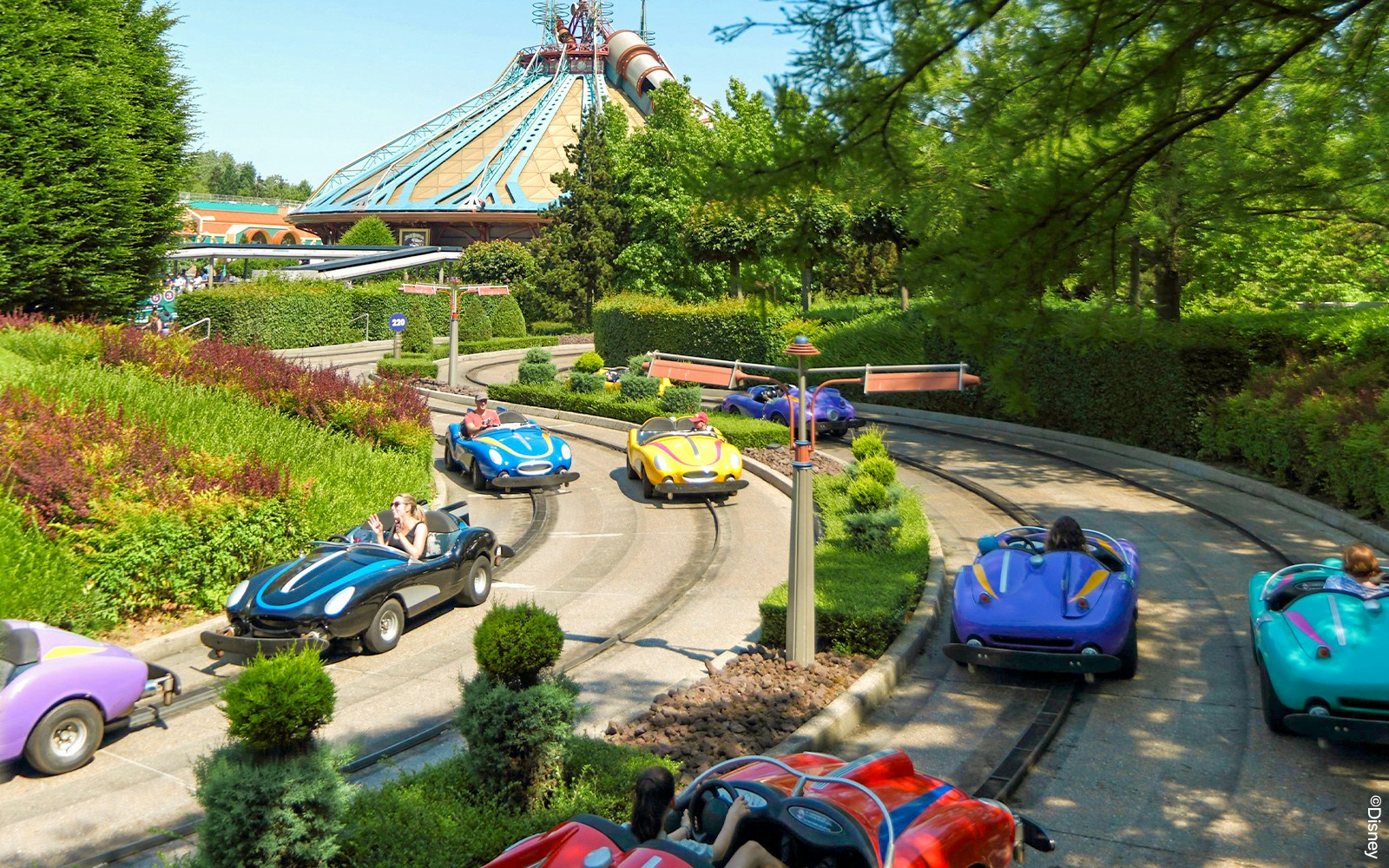 Visitors driving mini cars on the Autopia track at Disneyland Paris.