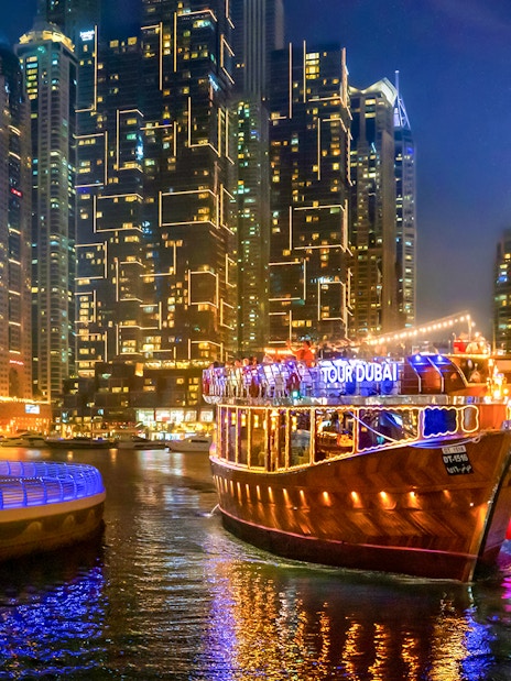 Luxury dhow cruise on Dubai Marina promenade at night with city skyline.