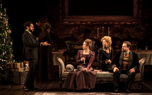 Theater scene from Leopoldstadt with actors in period costumes sitting on a sofa near a decorated Christmas tree.