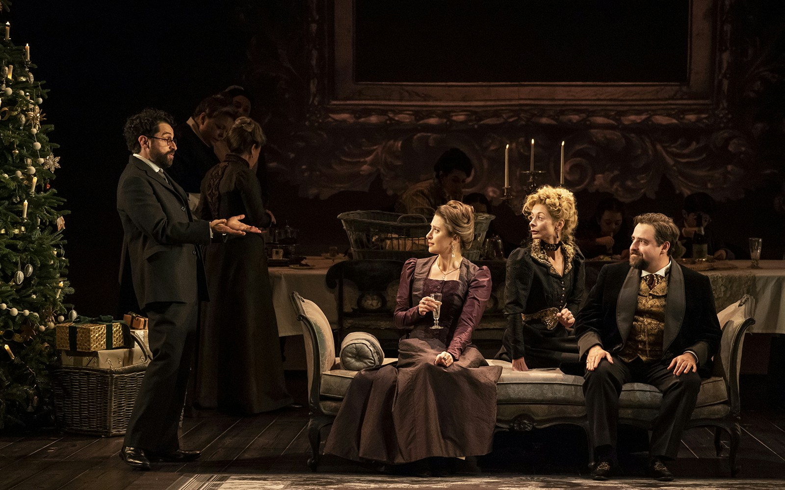 Theater scene from Leopoldstadt with actors in period costumes sitting on a sofa near a decorated Christmas tree.