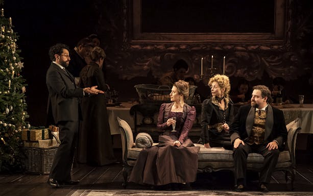 Theater scene from Leopoldstadt with actors in period costumes sitting on a sofa near a decorated Christmas tree.