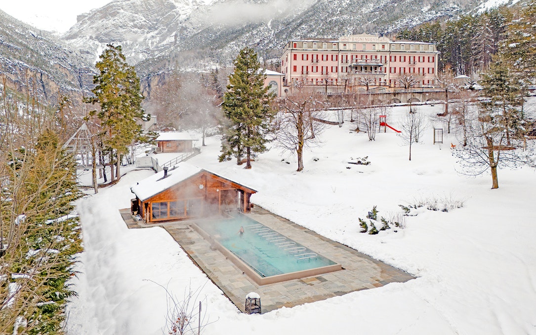 Outdoor thermal pool at QC Terme Bagni Nuovi di Bormio surrounded by snowy landscape.