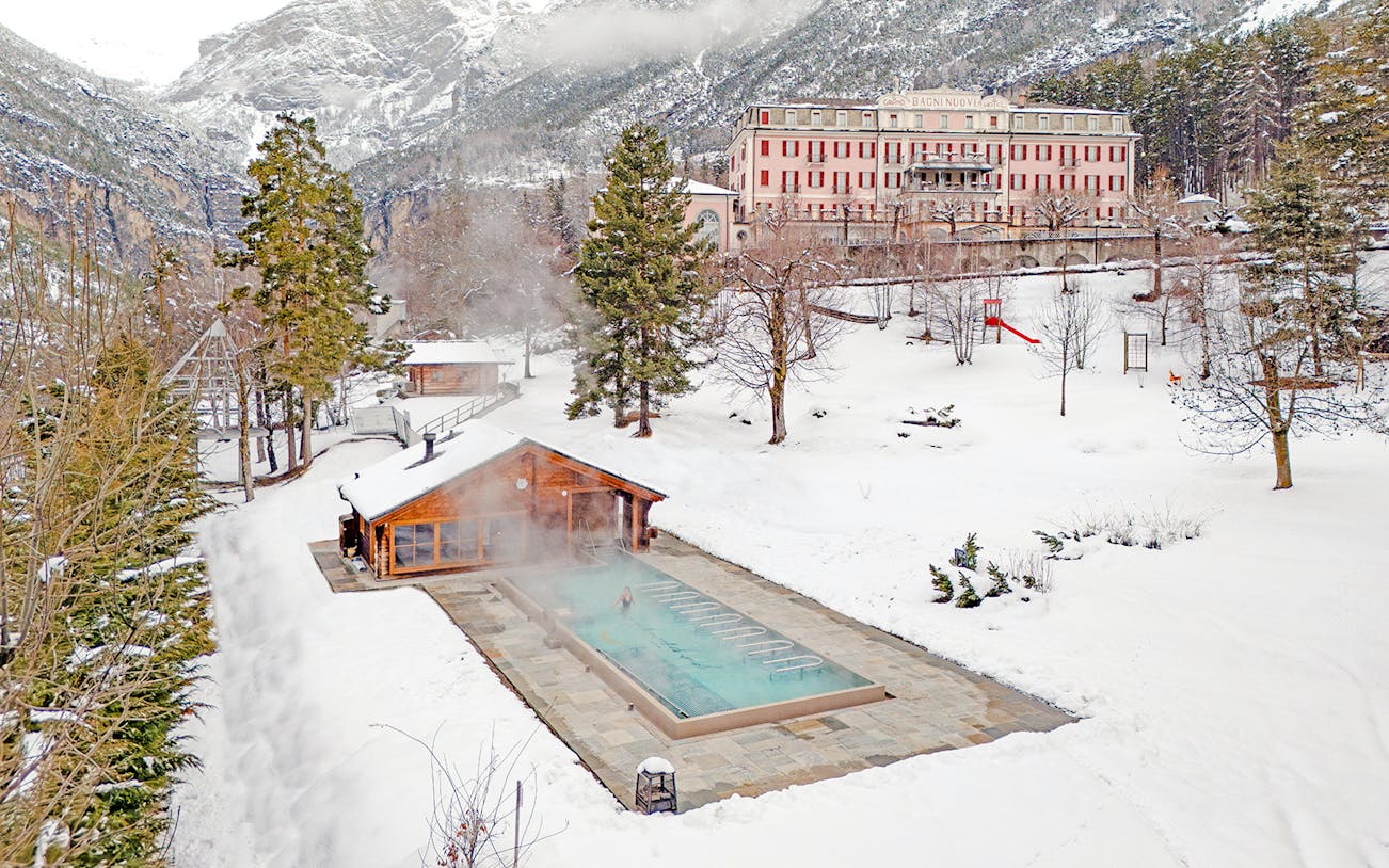 Outdoor thermal pool at QC Terme Bagni Nuovi di Bormio surrounded by snowy landscape.