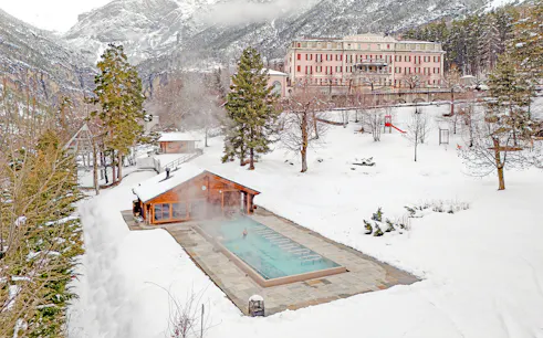 Outdoor thermal pool at QC Terme Bagni Nuovi di Bormio surrounded by snowy landscape.