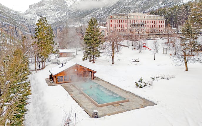 Outdoor thermal pool at QC Terme Bagni Nuovi di Bormio surrounded by snowy landscape.