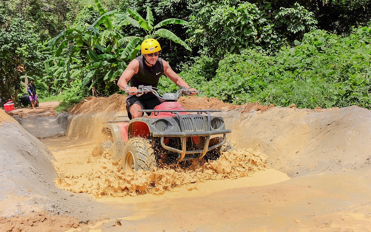 ATV rider navigating muddy trail in Phuket jungle.
