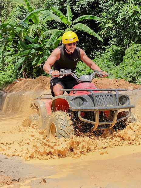 ATV rider navigating muddy trail in Phuket jungle.