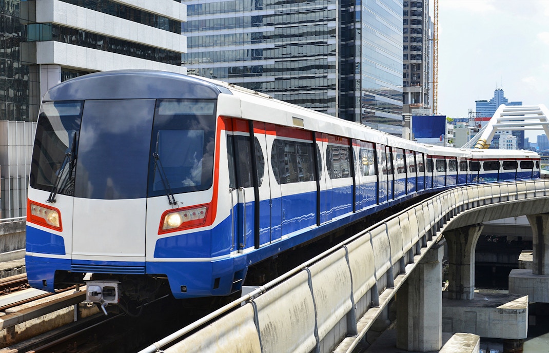 Sky train traveling through Bangkok cityscape with skyscrapers in the background.