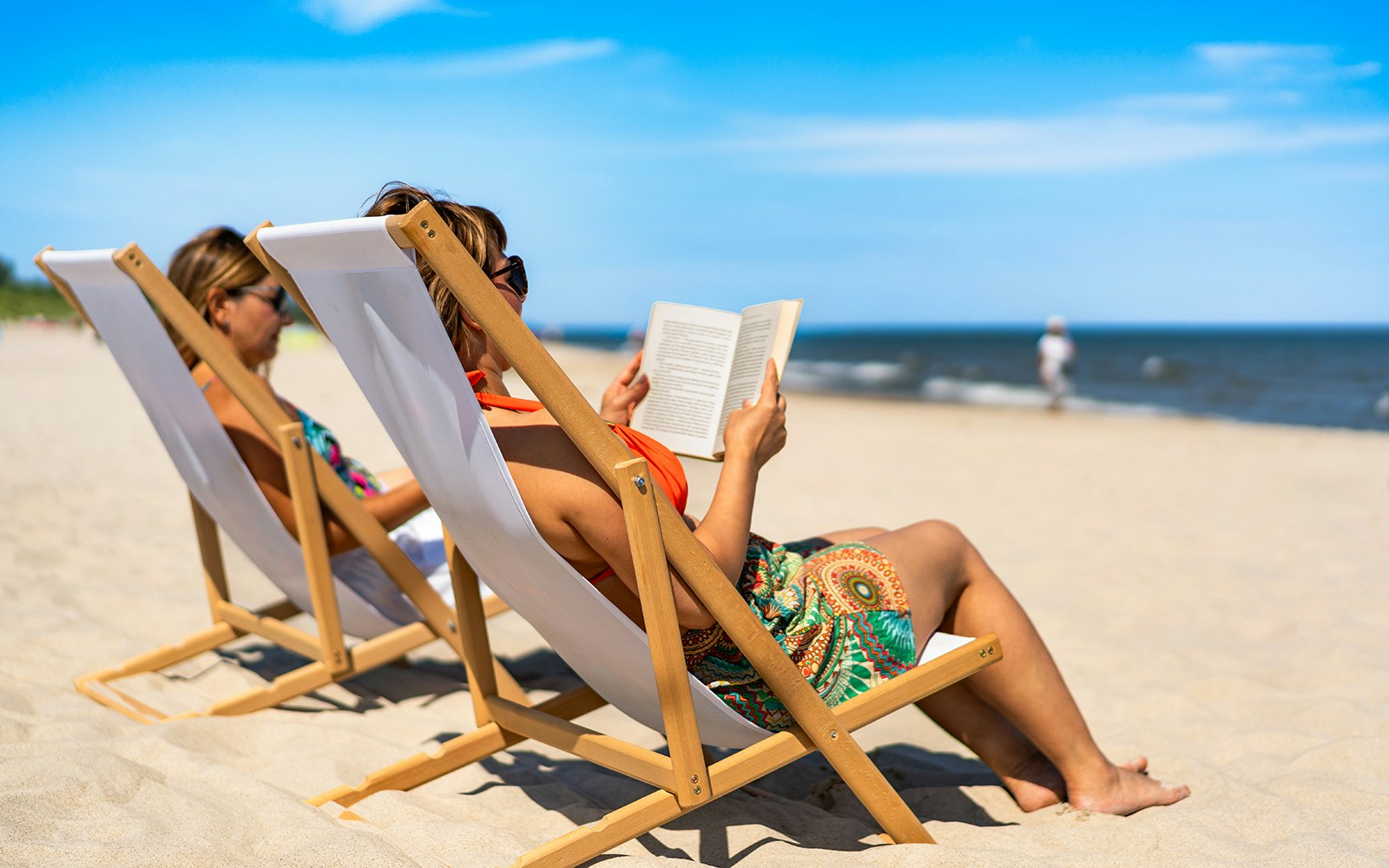 Two women on beach chairs reading books by the ocean.
