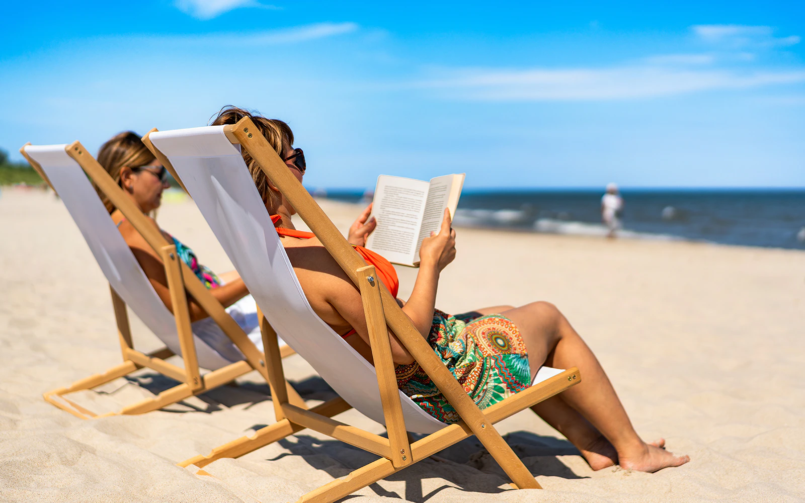 Two women on beach chairs reading books by the ocean.