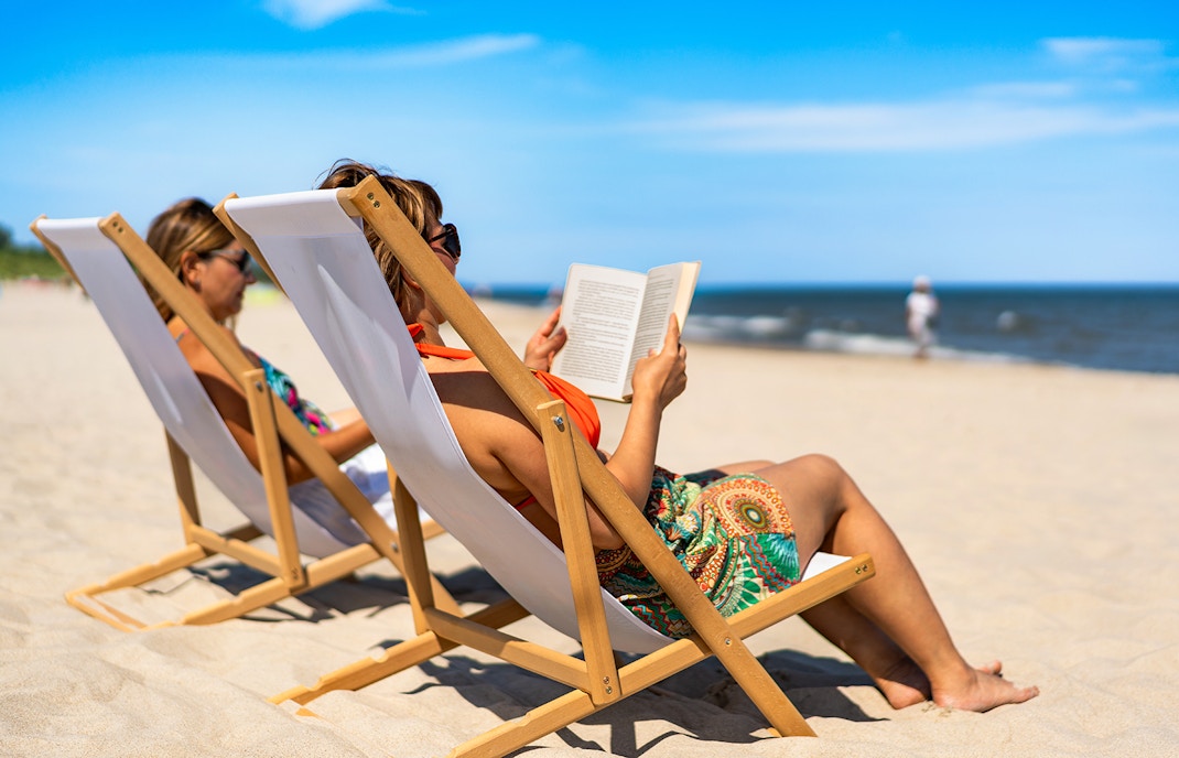 Two women on beach chairs reading books by the ocean.