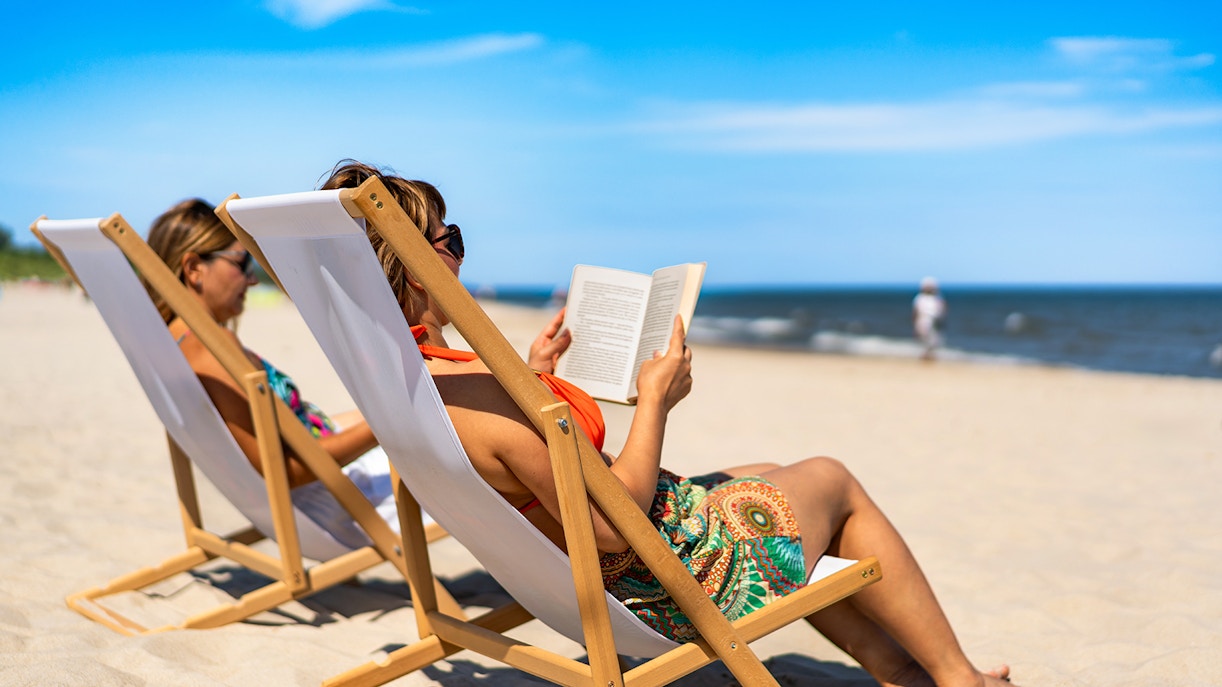 Two women reading books while sunbathing on a sandy beach in Barcelona, Spain.