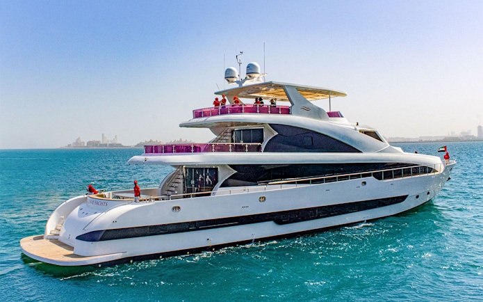 Superyacht TriDeck cruising in clear blue waters near a distant city skyline.
