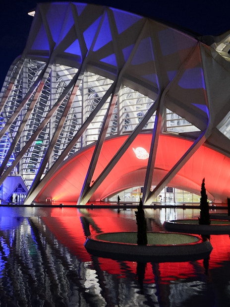 Hemisfèric and Science Museum Valencia illuminated at night, reflecting in water.