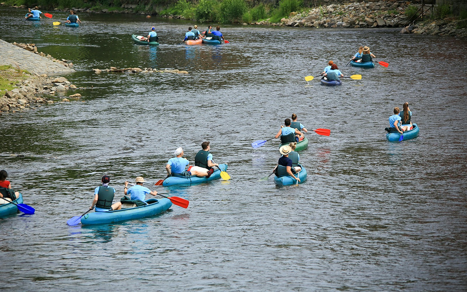 Group rafting on Vltava River, Czech Republic, with colorful paddles and inflatable rafts.