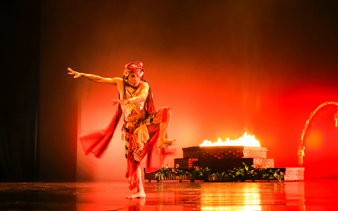 Performer in traditional costume at Devdan Show, Bali, with fire-lit stage backdrop.