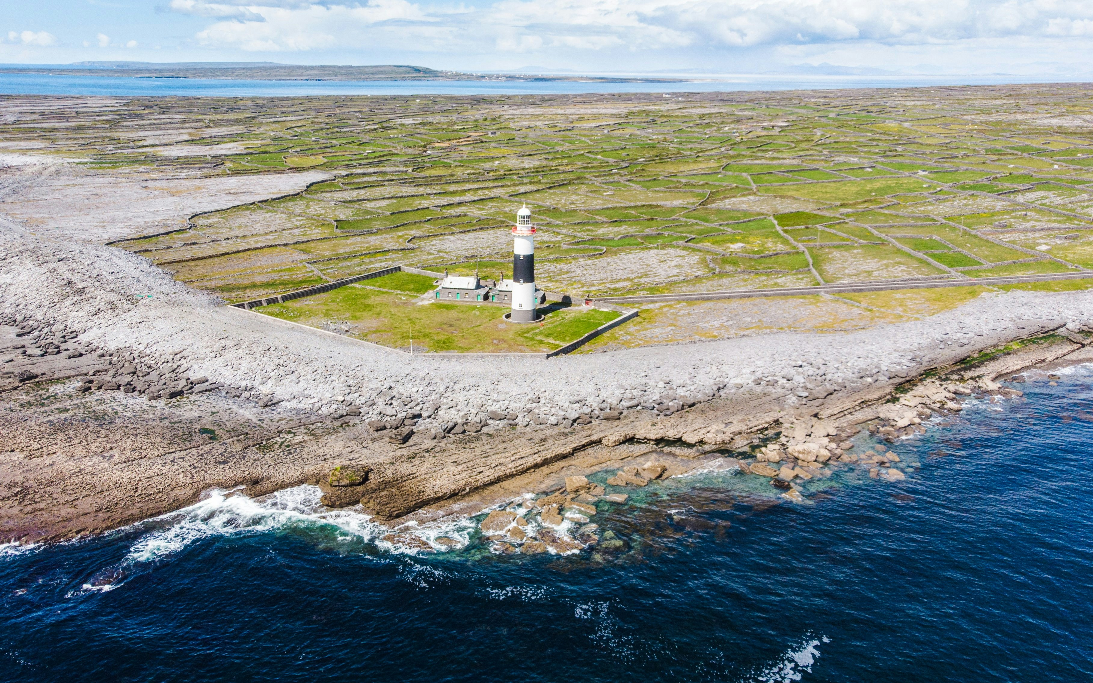 Aerial view of a lighthouse on the Aran Islands, surrounded by rocky coastline and green fields.