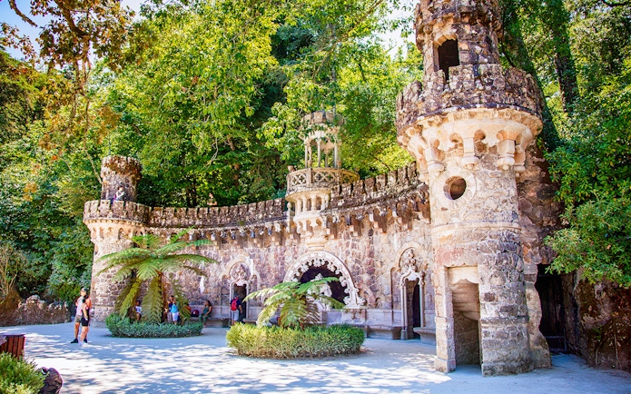 Quinta da Regaleira stone tower and archway surrounded by lush greenery, Sintra, Portugal.