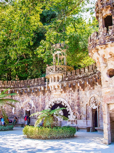 Quinta da Regaleira stone tower and archway surrounded by lush greenery, Sintra, Portugal.