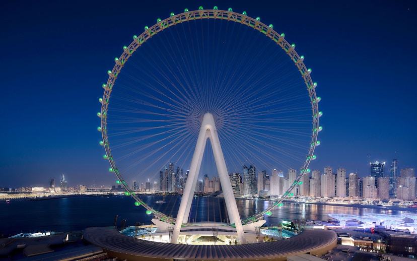 Ain Dubai illuminated at night with city skyline in the background.