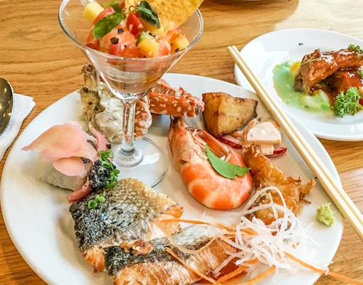 Catamaran sailing near Santorini coastline with passengers enjoying lunch on deck.