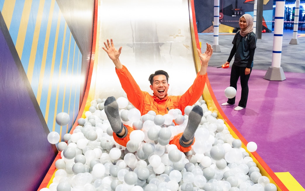Visitor sliding into ball pit at indoor playground.