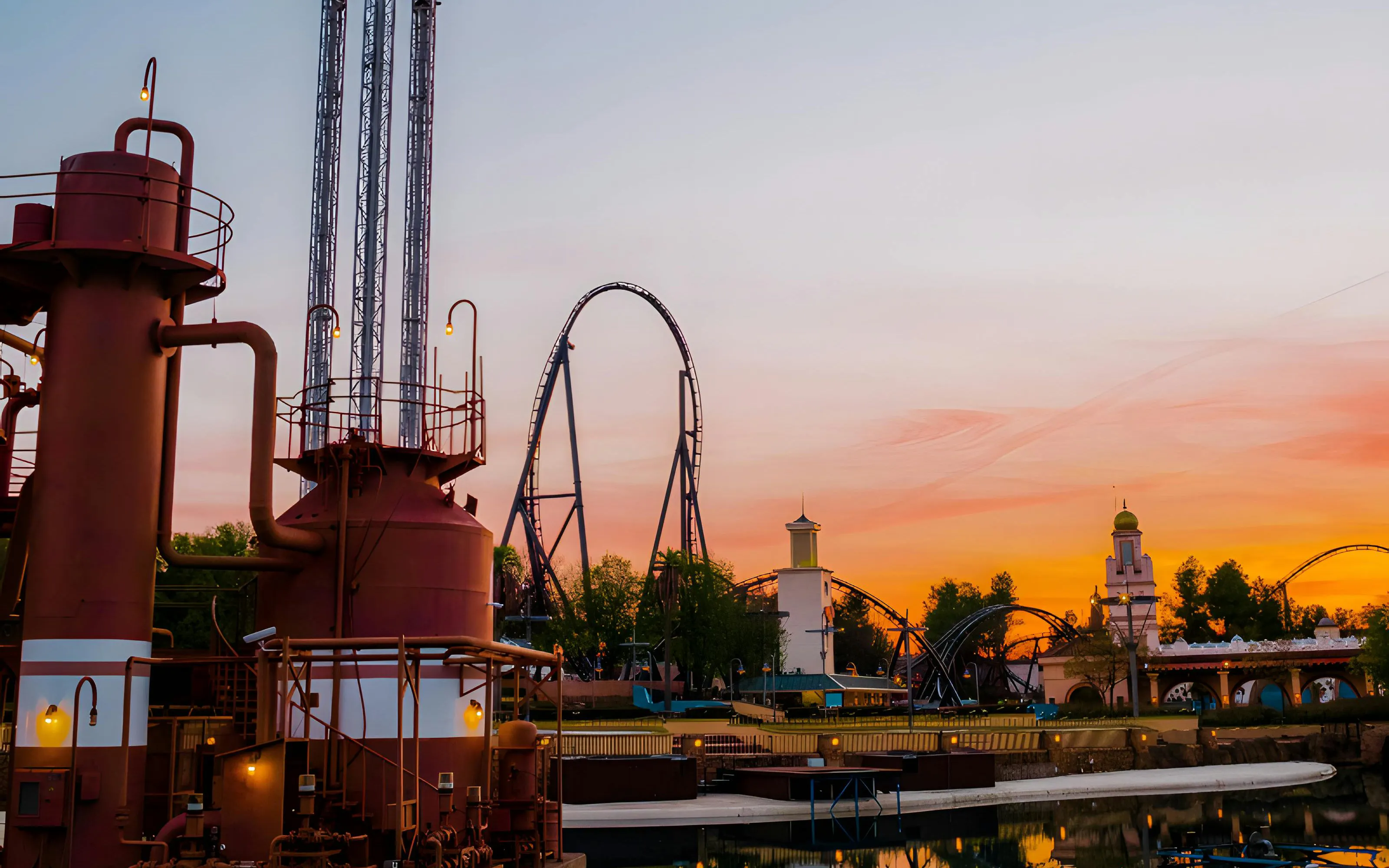 Parque Warner roller coaster at sunset with industrial structures in foreground.