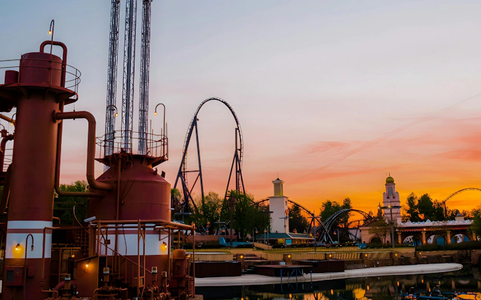 Parque Warner roller coaster at sunset with industrial structures in foreground.