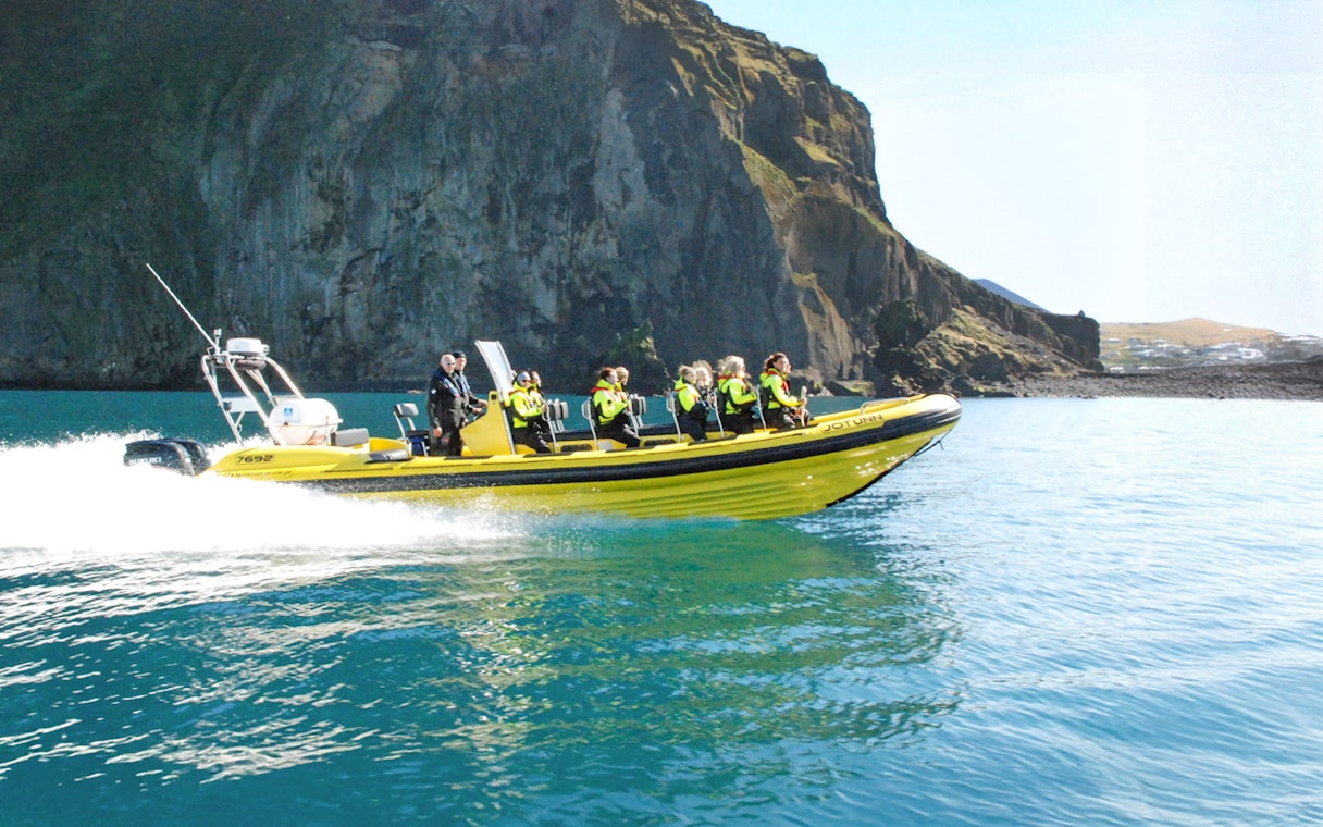 Guests on a RIB speedboat tour in Reykjavik, Iceland, near rocky cliffs.
