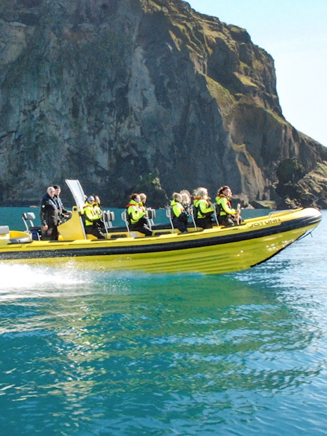 Guests on a RIB speedboat tour in Reykjavik, Iceland, near rocky cliffs.