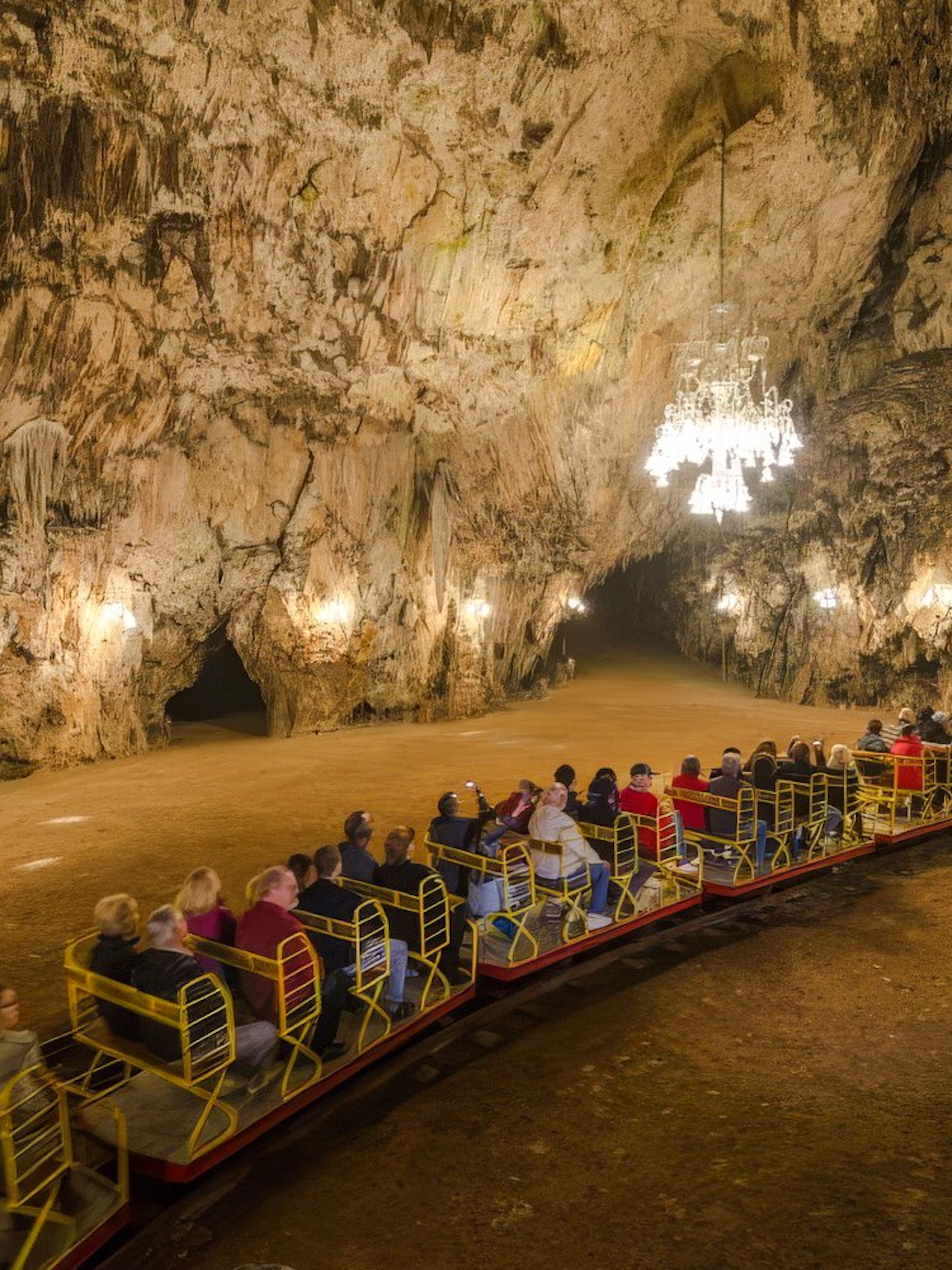 Guests on a train exploring Postojna Cave's illuminated chambers.