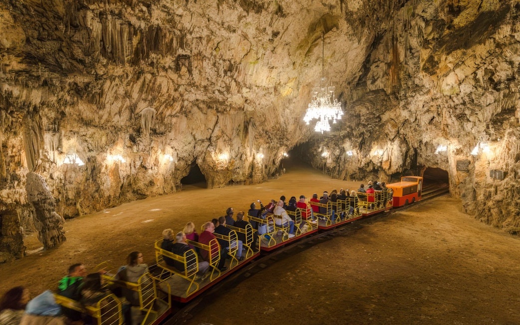 Guests on a train exploring Postojna Cave's illuminated chambers.