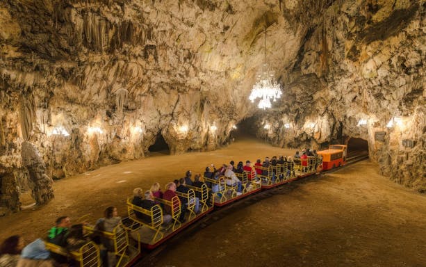Guests on a train exploring Postojna Cave's illuminated chambers.