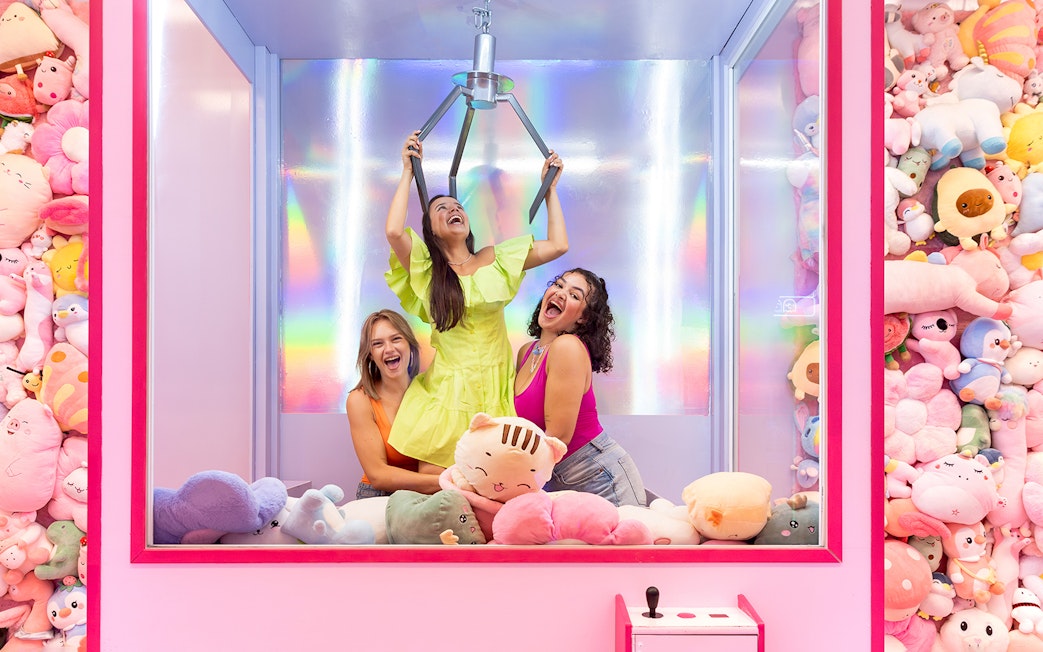 Women enjoying a claw machine game surrounded by plush toys in Liverpool.