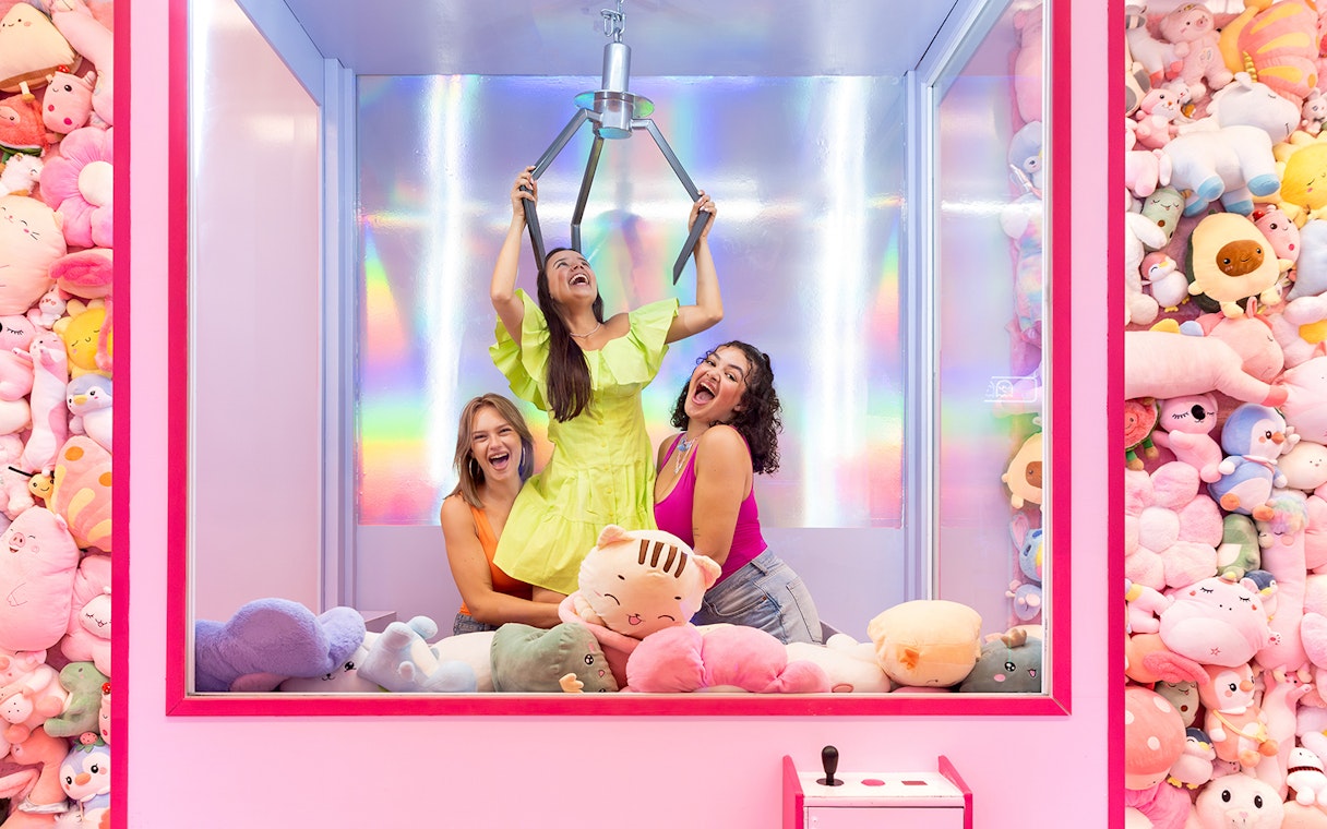 Women enjoying a claw machine game surrounded by plush toys in Liverpool.