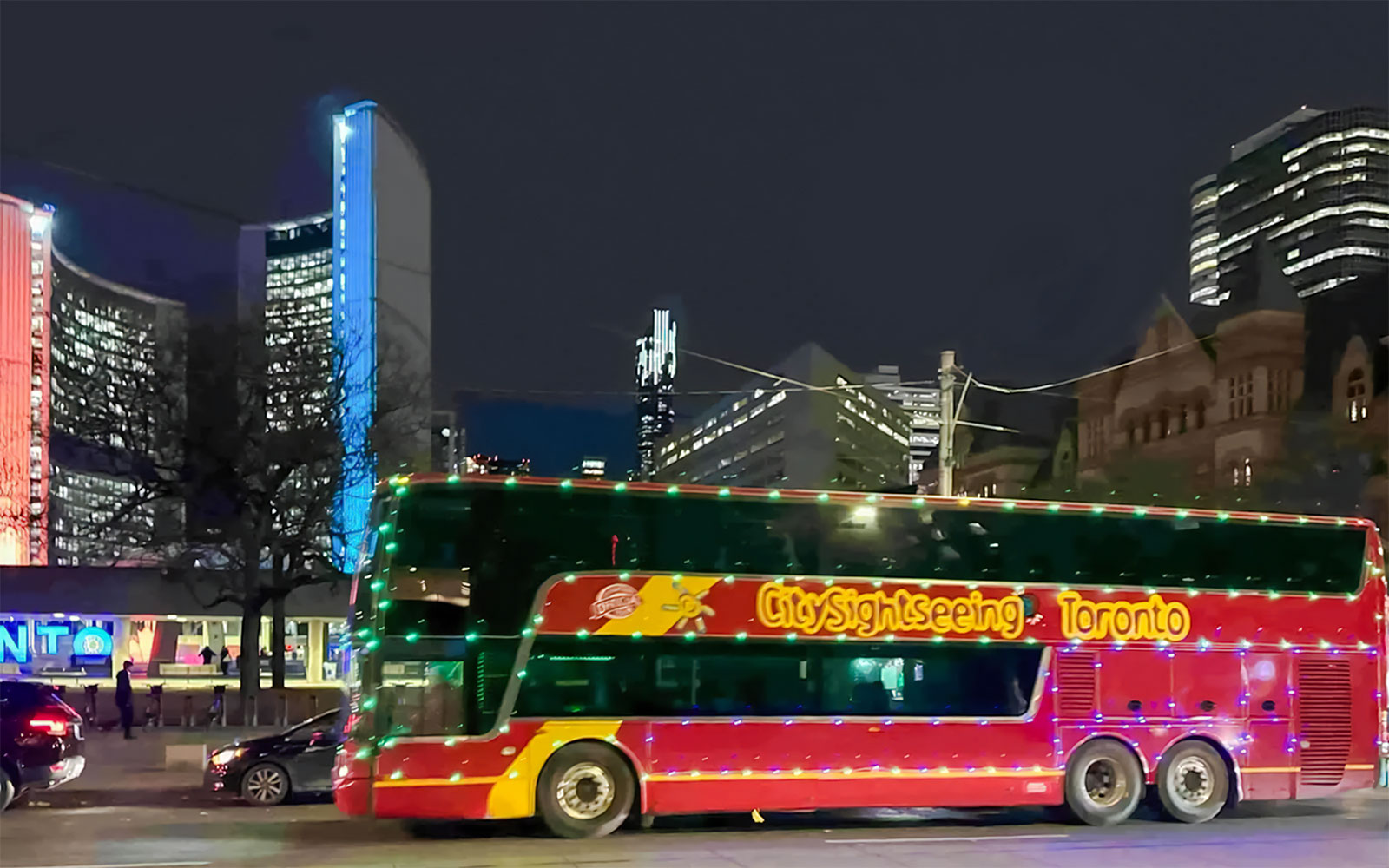 City Sightseeing bus in Toronto at night with illuminated buildings in the background.