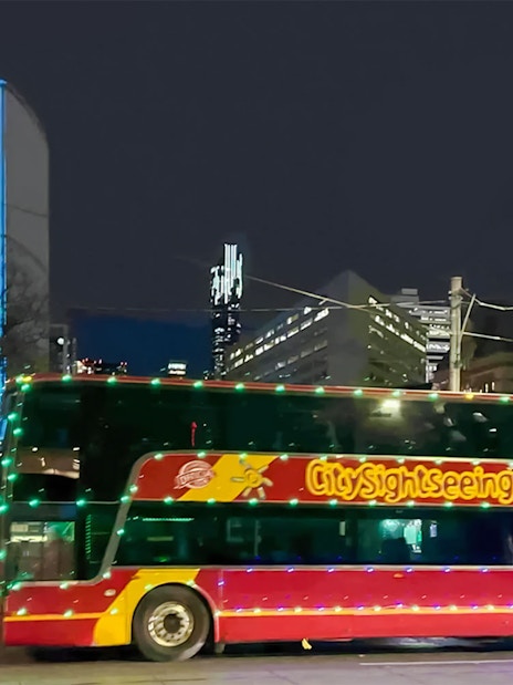 City Sightseeing bus in Toronto at night with illuminated buildings in the background.