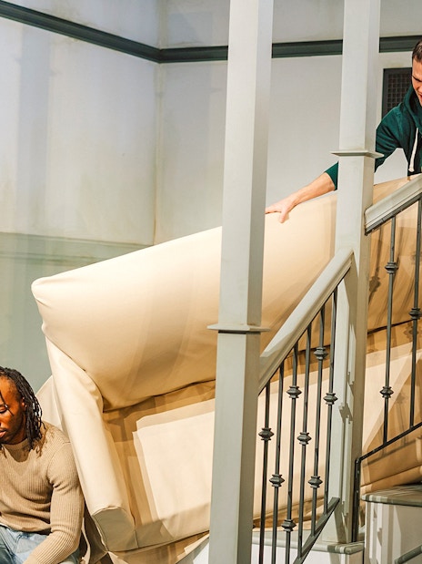 Two people maneuvering a couch on a staircase at The FRIENDS™ Experience.