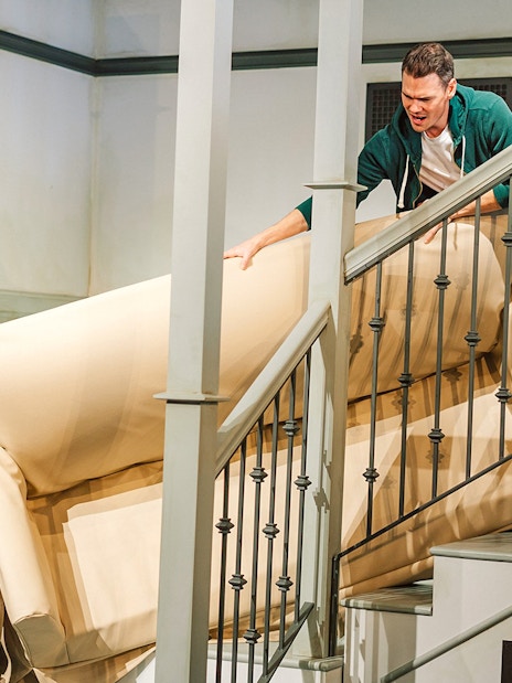 Two people maneuvering a couch on a staircase at The FRIENDS™ Experience.