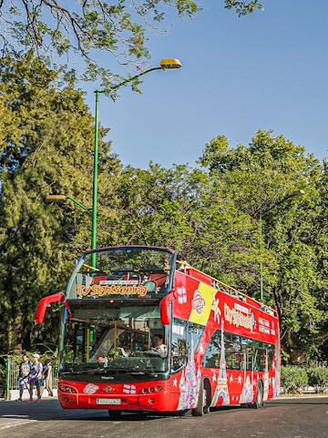 Red double-decker sightseeing bus in Budapest with tourists on board.