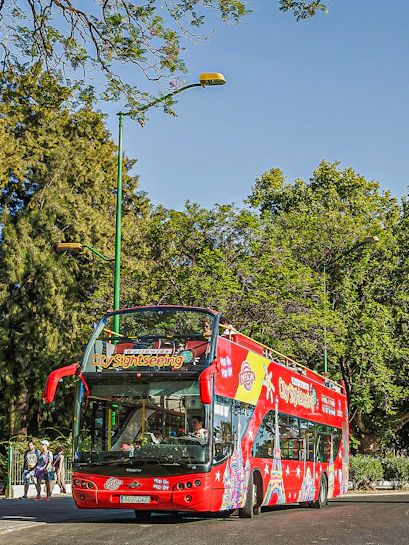 Red double-decker sightseeing bus in Budapest with tourists on board.
