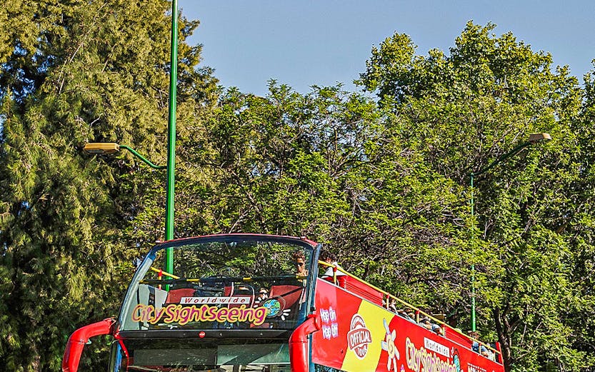 Red double-decker sightseeing bus in Budapest with tourists on board.