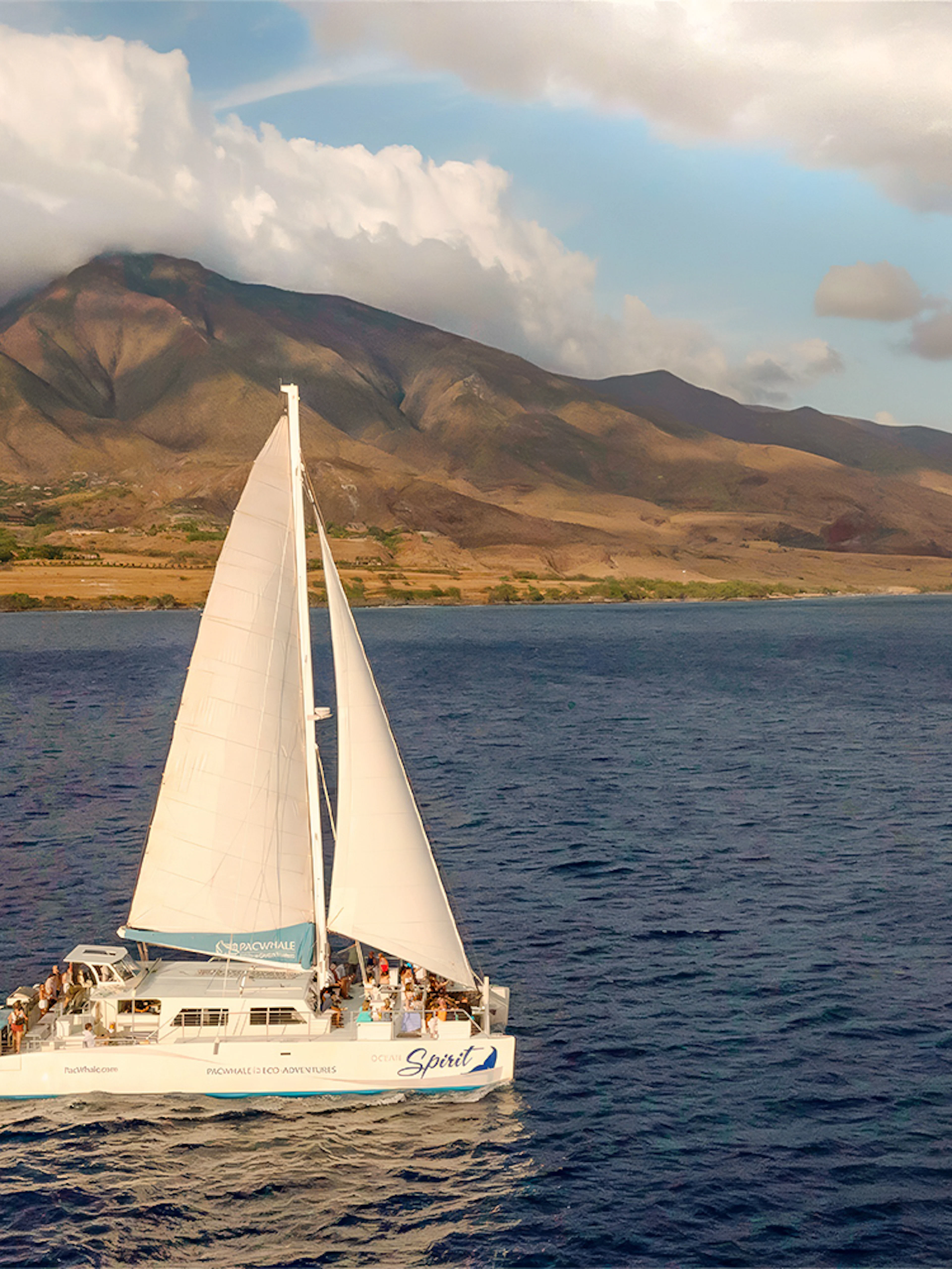 Sailboat on a sunset whale watching tour near Maui, Hawaii with mountains in the background.