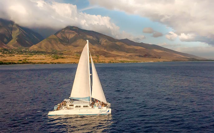 Sailboat on a sunset whale watching tour near Maui, Hawaii with mountains in the background.