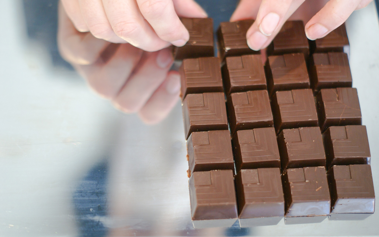 Hands arranging chocolate squares at Choco-Story Brussels Museum.