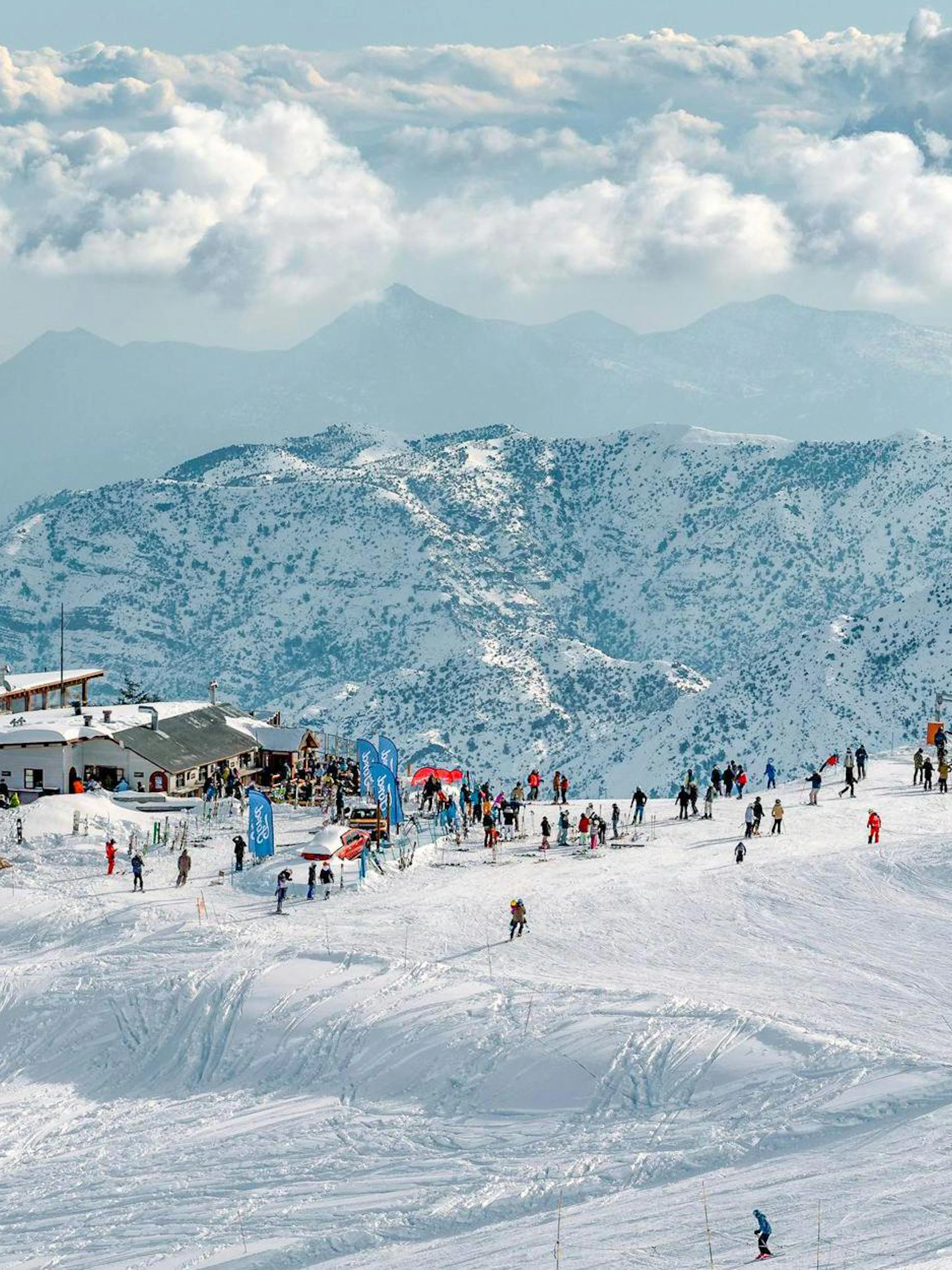 Tourists skiing and snowboarding at Farellones Park with snowy mountains in the background.